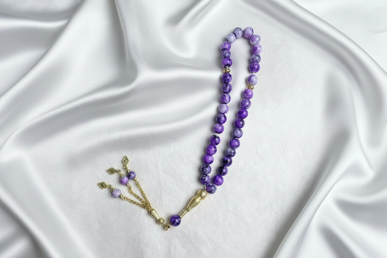 Tasbih de 33 perles de 10mm aux nuances de violet marbré et blanc, avec séparateurs dorés et pompon luxueux à chaînettes dorées.
