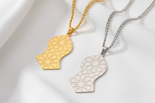 Collier en acier inoxydable avec pendentif Nalain Shareef orné de motifs d'étoiles géométriques islamiques, disponible en argent et or, présenté sur un drapé de soie blanche.