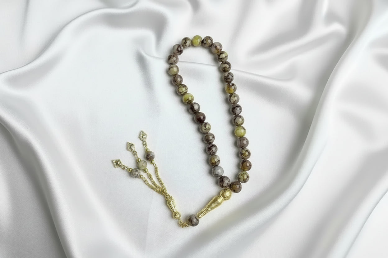 Tasbih de 33 perles de 10mm aux motifs marbrés jaune, marron et gris, avec séparateurs dorés et un grand pompon luxueux à chaînettes.