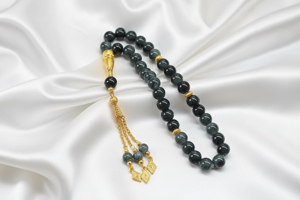 Tasbih de 33 perles de 10mm gris anthracite marbré avec des reflets brillants, séparateurs dorés ciselés et pompon luxueux doré avec pendentifs losanges.