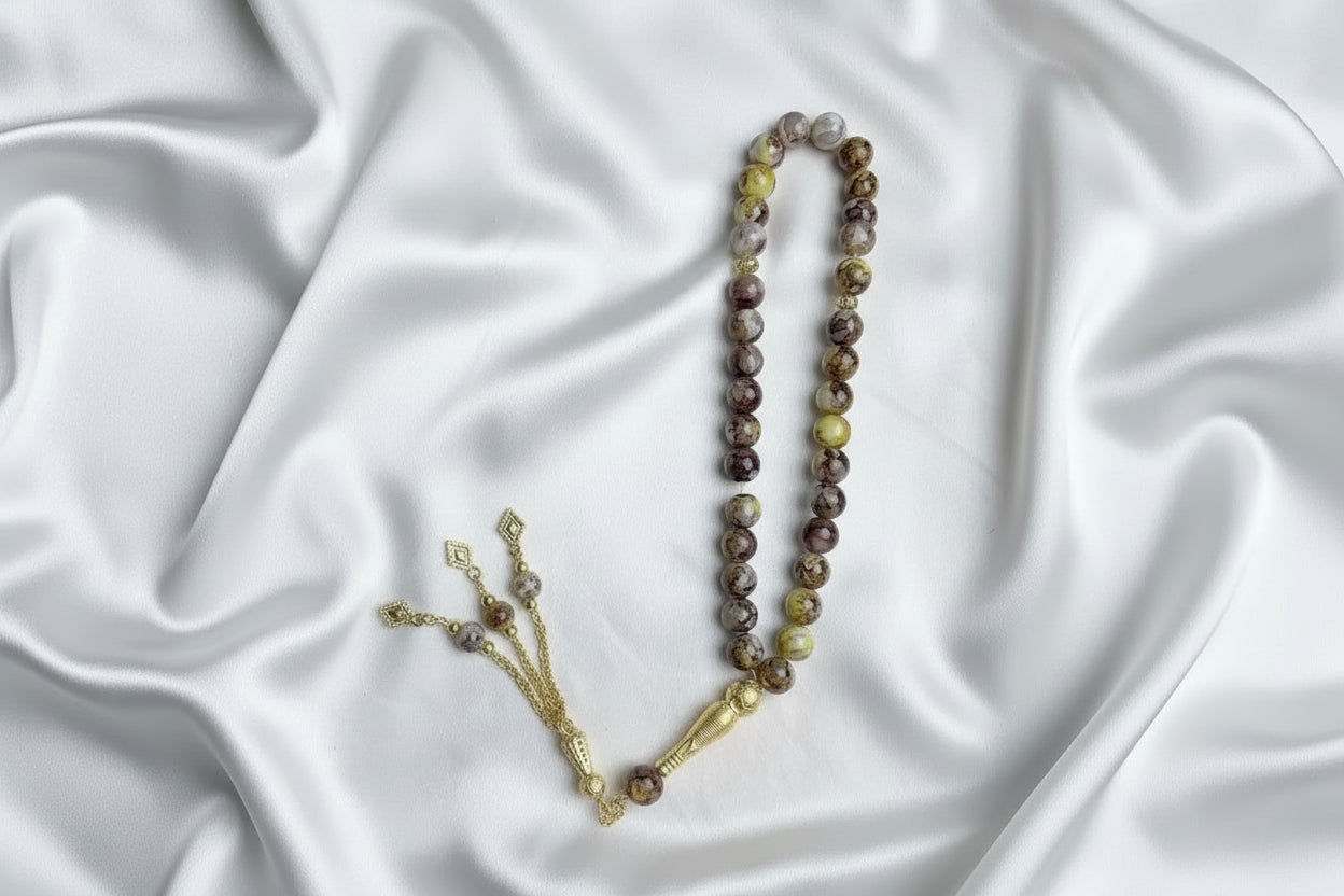Tasbih de 33 perles de 10mm aux nuances marbrées de jaune, beige et marron, avec séparateurs dorés et pompon artisanal doré à trois chaînettes.