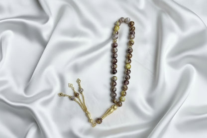Tasbih de 33 perles de 10mm aux nuances marbrées de jaune, beige et marron, avec séparateurs dorés et pompon artisanal doré à trois chaînettes.
