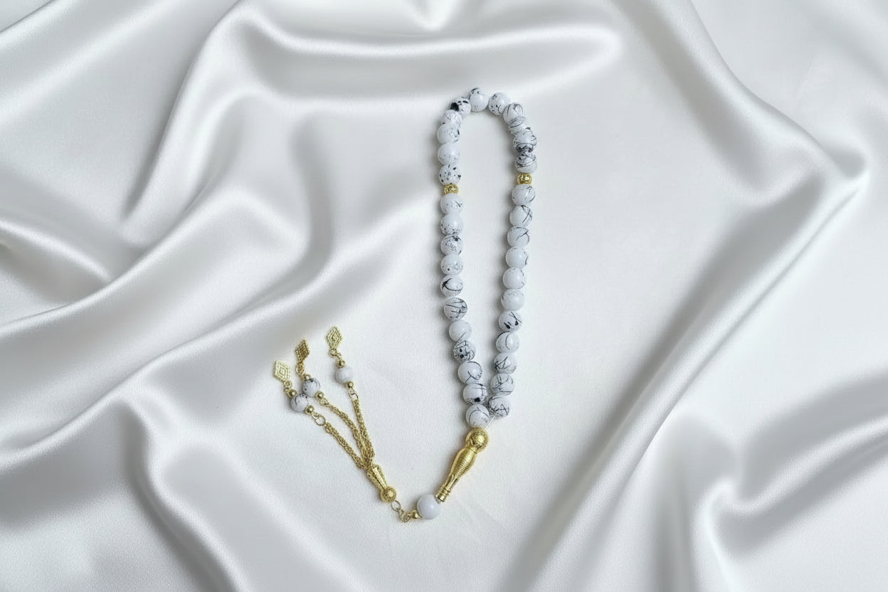 Tasbih de 33 perles de 10mm blanc marbré de noir, avec séparateurs dorés et pompon artisanal doré à trois chaînettes.