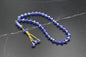 Tasbih élégant composé de 33 perles en cristal bleu saphir facettées, séparateurs dorés sertis de strass et pompon traditionnel à trois chaînettes dorées sur fond sombre.